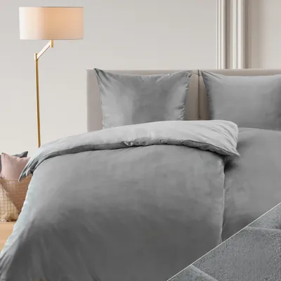 A bed with gray bedding and pillows, next to a floor lamp.