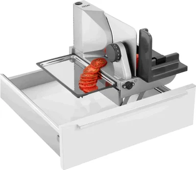 A slicer with sliced tomatoes on a tray, placed on top of a white drawer.