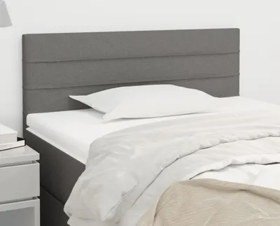 A close-up view of a dark gray fabric headboard for a bed, with a white pillow and bedding.