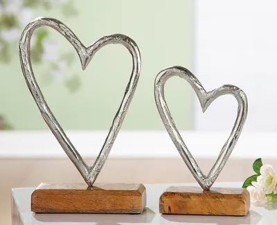 Two decorative metal hearts on wooden bases, with a blurred green background and a hint of flowers.