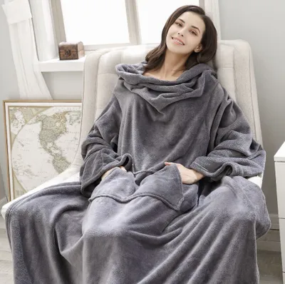A woman is sitting in a chair, wrapped in a large, gray blanket with sleeves.