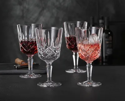 Four crystal wine glasses filled with red and pink wine, set on a dark surface with a dark, textured background.
