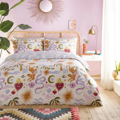 A bedroom scene with a bed dressed in a colorful duvet set, a bedside table with a lamp and vase, and a large plant.