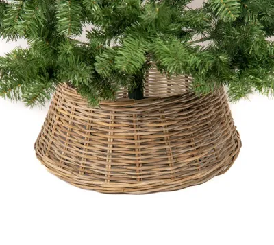 A close-up view of the base of a Christmas tree, showing the green branches and a woven rattan tree skirt.