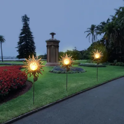 Solar garden lights shaped like suns are illuminating a garden path at dusk.