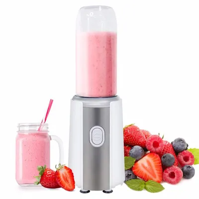 A portable blender filled with a pink smoothie, surrounded by fresh berries and a glass of smoothie.