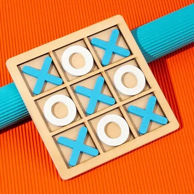 A wooden tic-tac-toe board with blue X's and white O's, placed on an orange textured surface with a blue ribbed object behind it.