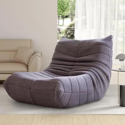 A gray beanbag chair is placed in a living room setting next to a sofa and a side table with a lamp.