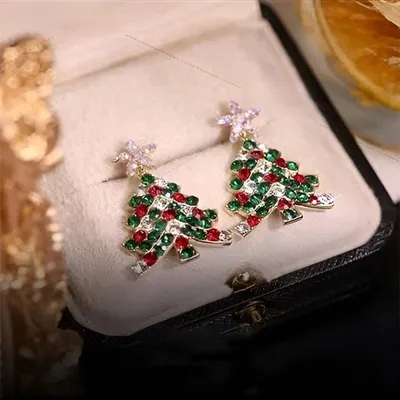 Paar goldene Weihnachtsbaum-Ohrringe mit roten, grünen und klaren Strasssteinen, mit Sternaufsatz, präsentiert in einer beigen Schmuckbox