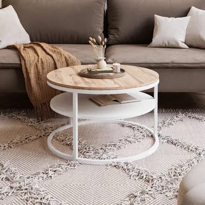 A round coffee table with a wooden top and a white shelf, placed on a patterned rug in a living room setting.