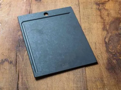 A black cutting board with a juice groove is placed on a wooden surface.