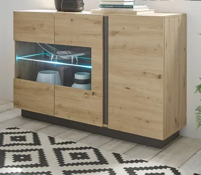 A modern sideboard with a glass-fronted cabinet displaying decorative items and illuminated by blue LED lights, placed on a wooden floor with a patterned rug.
