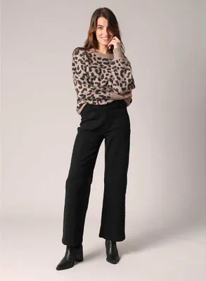 A woman is posing in a studio setting, wearing a leopard print sweater and black pants.