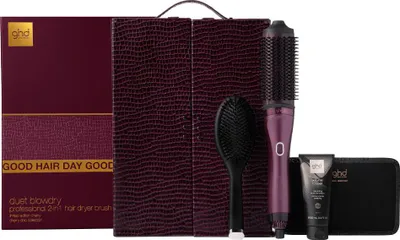 A gift set containing a hair dryer brush, a styling brush, a heat-resistant mat, and a tube of hair product, presented in a burgundy textured case.