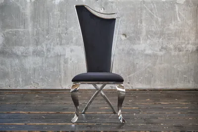 A black velvet dining chair with a silver frame is shown against a concrete wall and wooden floor.