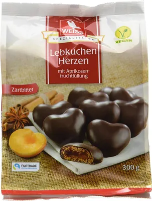 A package of heart-shaped chocolate-covered lebkuchen with apricot filling, along with some ingredients like star anise, cinnamon sticks, and an apricot half.