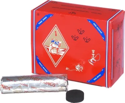 A red box of hookah charcoal with a roll of charcoal and a single piece of charcoal in front of it.