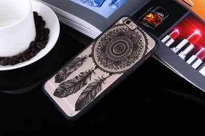 A phone case with a dreamcatcher design is placed on a table next to a cup of coffee and some books.
