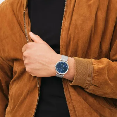A person wearing a brown jacket and a black shirt, showing a silver watch with a blue dial on their wrist.