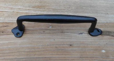 A black metal handle is placed on a wooden surface.