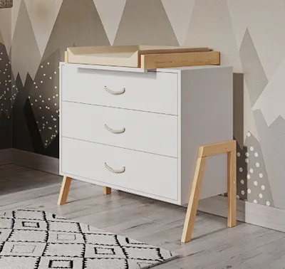 A white dresser with a wooden changing table attachment, set against a mountain-themed wallpaper.