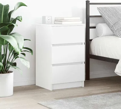 A white three-drawer nightstand is shown next to a bed in a bedroom setting.