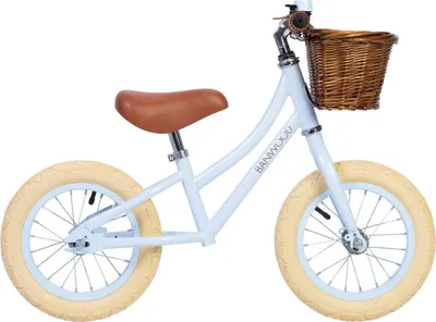 A light blue balance bike with a brown seat and a wicker basket on the handlebars, shown against a white background.