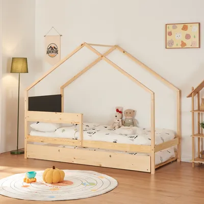 A children's house-shaped bed with a pull-out trundle bed, set up in a room with a floor lamp, a rug, and wall decor.