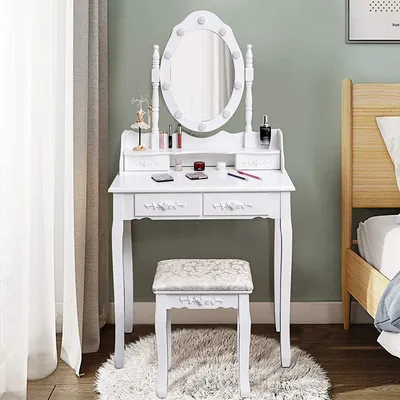 A white vanity table with a lighted mirror and a stool is set up in a bedroom next to a bed and a window with sheer curtains.