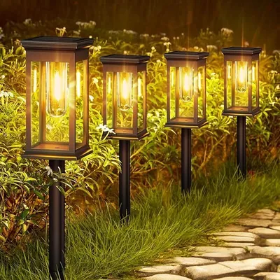 Four solar garden lights are illuminated at dusk, lining a stone pathway through a garden.