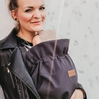A woman is holding a baby in a carrier, wearing a black leather jacket.