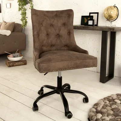 A brown tufted office chair with a black base and wheels is shown in a room with a sofa, a table with decorative items, and a rug.