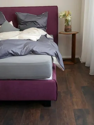 A close-up view of a bed with purple bedding and gray and white sheets.