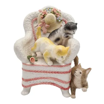 A ceramic figurine of kittens playing on a chair with a hat.