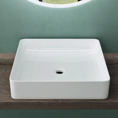 A white ceramic sink is placed on a wooden shelf against a light green wall.