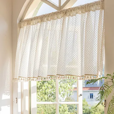 A sheer curtain with a diamond pattern and tassels hangs in a window.