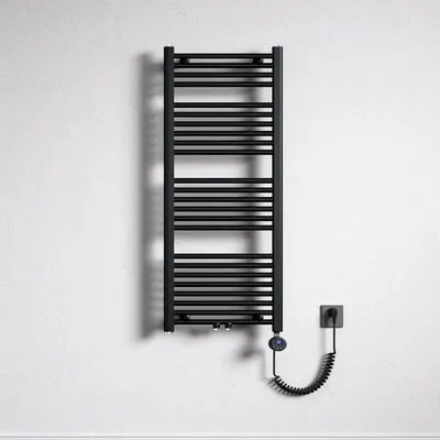 A black electric towel radiator mounted on a textured white wall, with a coiled power cord connecting to a wall socket.