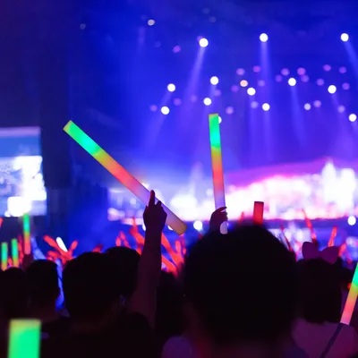 A crowd at a concert or event, holding up illuminated glow sticks.