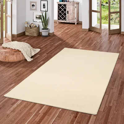 A cream-colored rug is placed on a wooden floor in a room with natural light coming from open doors.