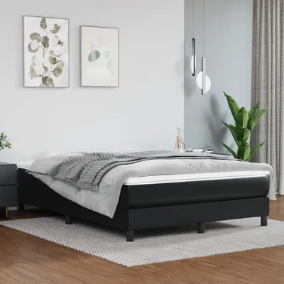 A black bed frame with a mattress and bedding, set in a minimalist bedroom with artwork on the wall and a plant.