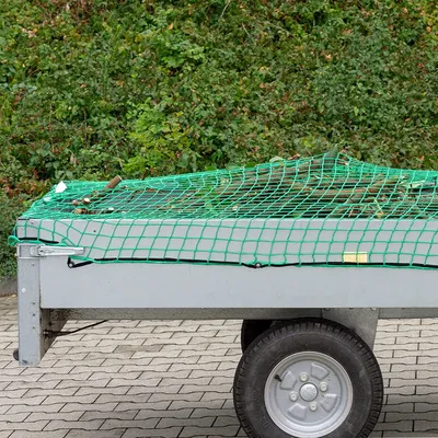A trailer covered with a green net, filled with branches and debris.