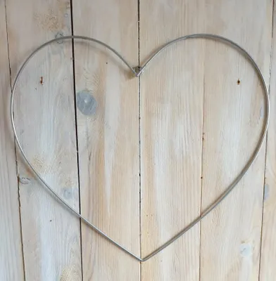 A silver metal heart-shaped wire frame is centered on a light-colored wooden plank background.