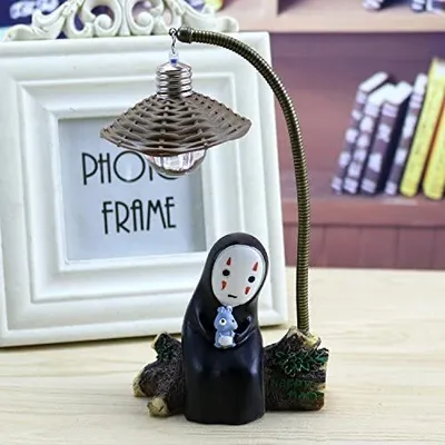 A decorative lamp with a figurine of the character No-Face from Spirited Away, placed in front of a white photo frame.