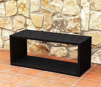 A black metal bench is placed on a tiled patio in front of a stone wall.