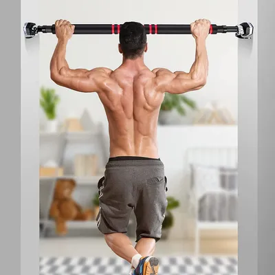 A muscular man is doing pull-ups on a pull-up bar mounted in a doorway, with a room in the background.