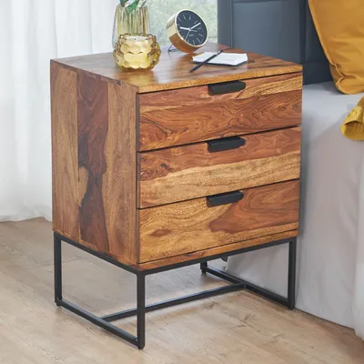 A wooden nightstand with three drawers and a black metal frame, placed next to a bed.