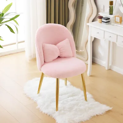 A pink fluffy chair with a bow cushion and gold legs sits on a white rug in front of a vanity table.