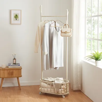 A clothing rack with clothes and a bag is placed next to a small wooden table with books and a mug, near a window with curtains.