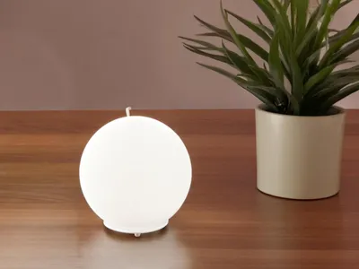 A white spherical lamp sits on a wooden surface next to a potted plant.