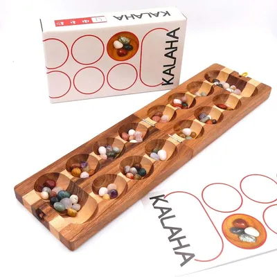 Kalaha-Steinchenspiel mit Verpackung und Anleitung; Holzbrett mit Mulden und farbigen Bohnensteinen dekorativ arrangiert.